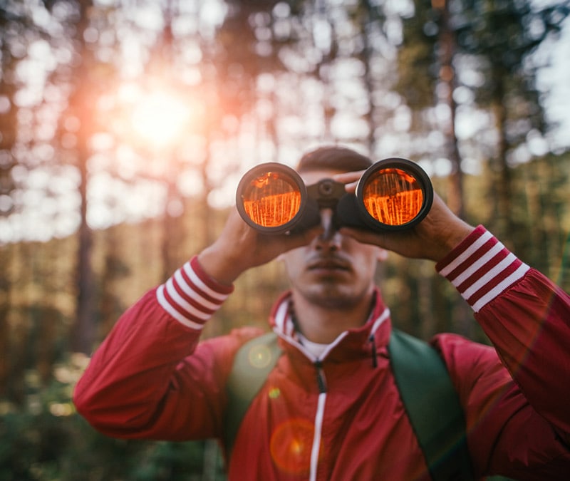 Ein Mann, der jemanden mit einem Fernglas ausspioniert.