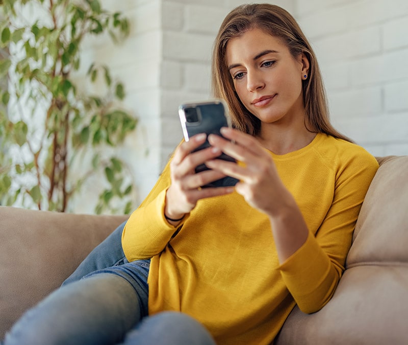 Eine Frau auf einem Sofa mit einem Smartphone, die recherchiert, wie man ein Instagram-Konto löscht