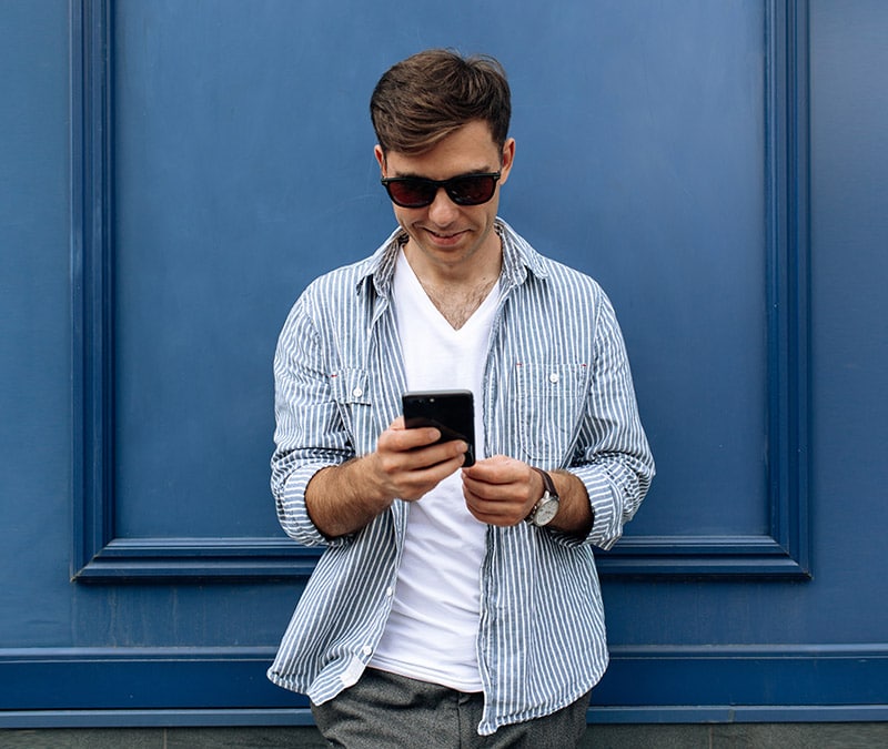 Ein junger Mann mit Sonnenbrille beim Überprüfen seines Smartphone, um herauszufinden, wie er sein Facebook-Konto löschen kann.