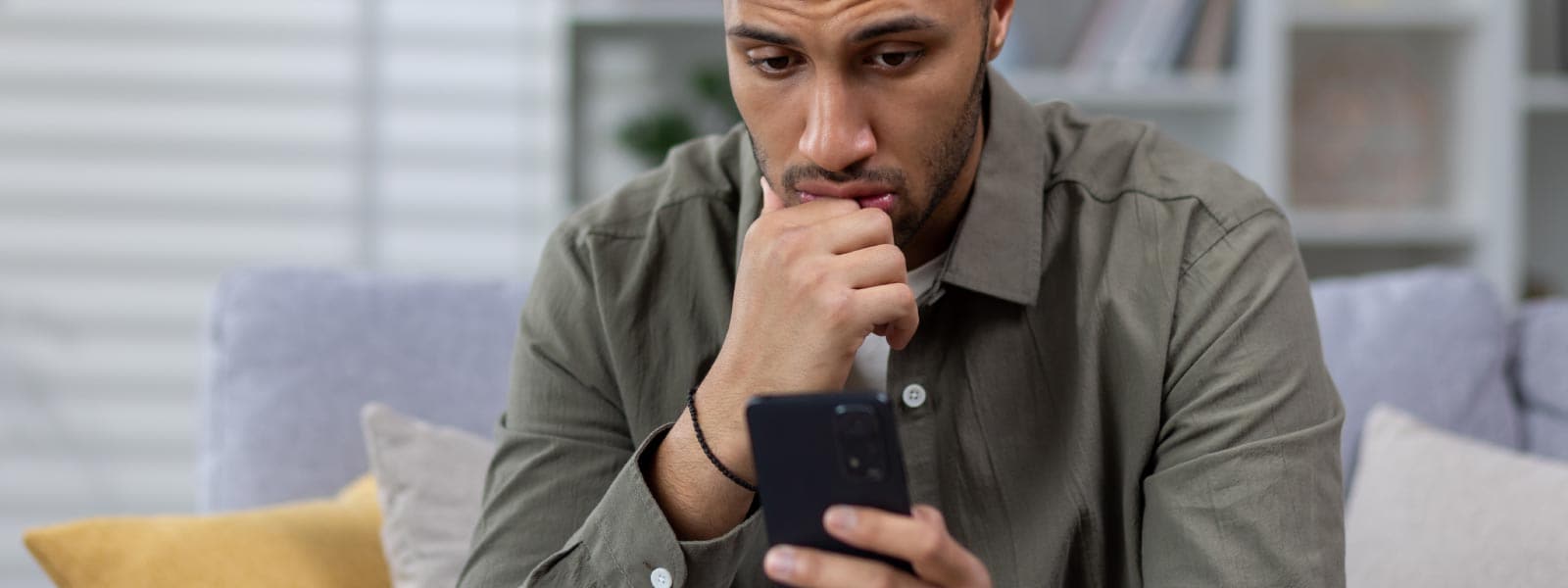 Ein Mann blickt besorgt auf sein Smartphone und fragt sich, ob es abgehört wird oder gehackt wurde.