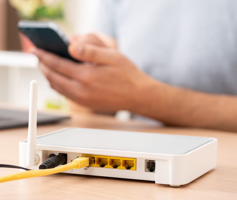 Eine Person, die ihr Telefon neben einem WLAN-Router benutzt und versucht, die Internetgeschwindigkeit zu erhöhen.