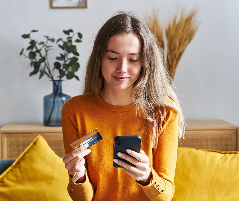 Eine junge Frau mit einer Kreditkarte und einem Smartphone, die darüber nachdenkt, wie sie ihren digitalen Fußabdruck beim Online-Shopping löschen kann.