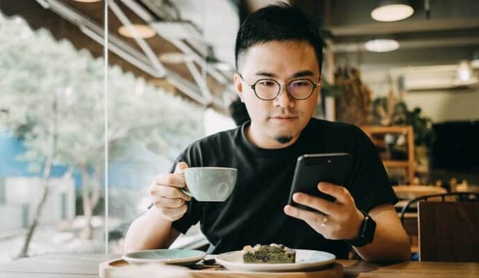Mann beim Kaffeetrinken mit Handy, auf dem Norton 360 Standard gestartet wird