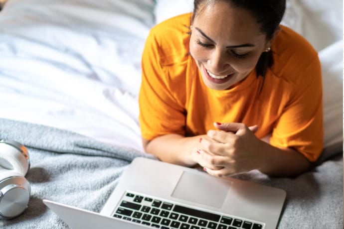 Lächelnde Frau im Bett mit Laptop