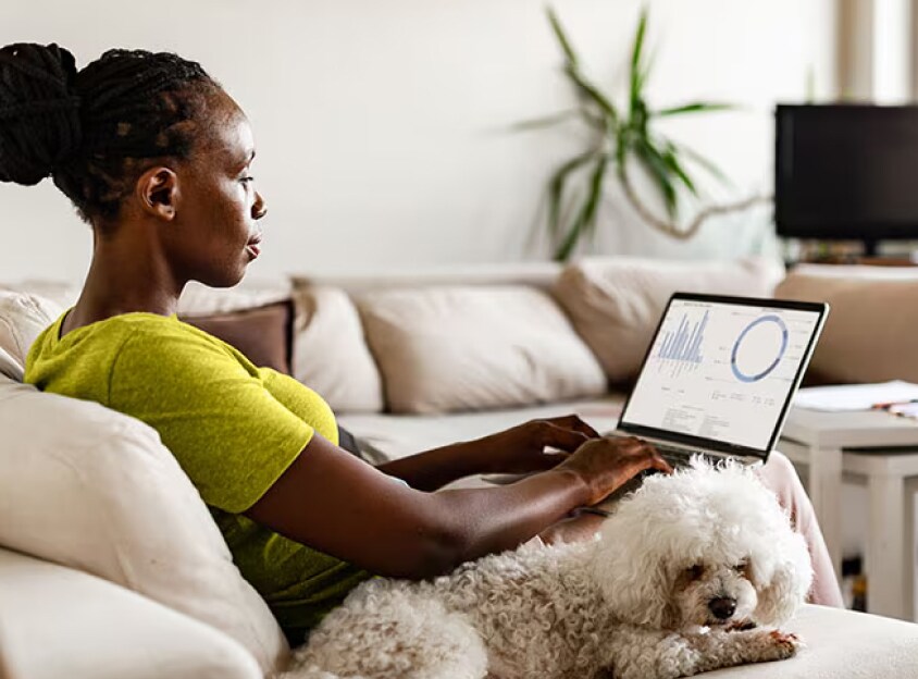 Sitzende Frau mit Hund, die am Laptop arbeitet