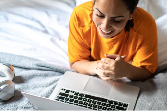 Lächelnde junge Frau im Bett mit Laptop.